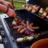 Chef cooking sausages and vegetables on BBQ skewers outdoors