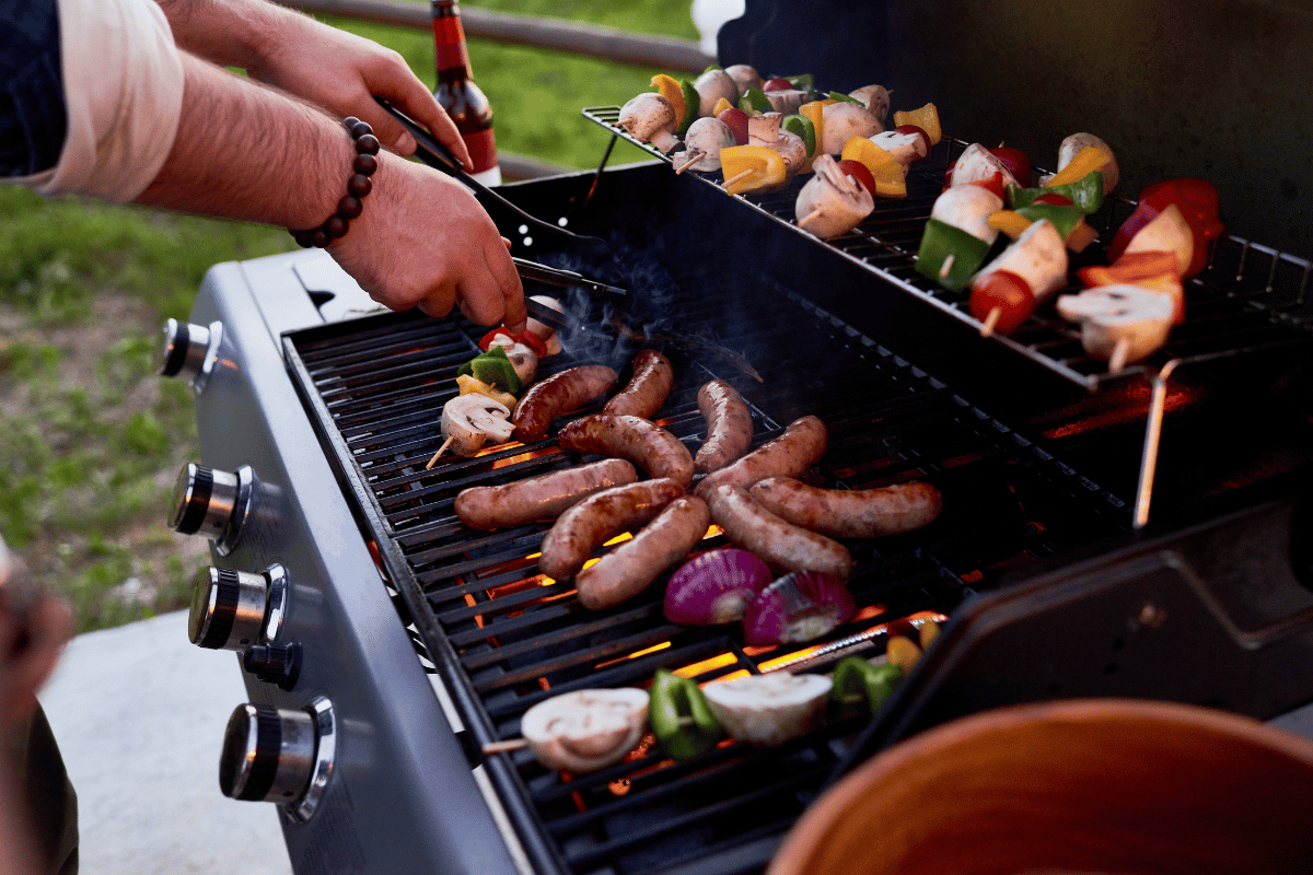 Chef cooking sausages and vegetables on BBQ skewers outdoors