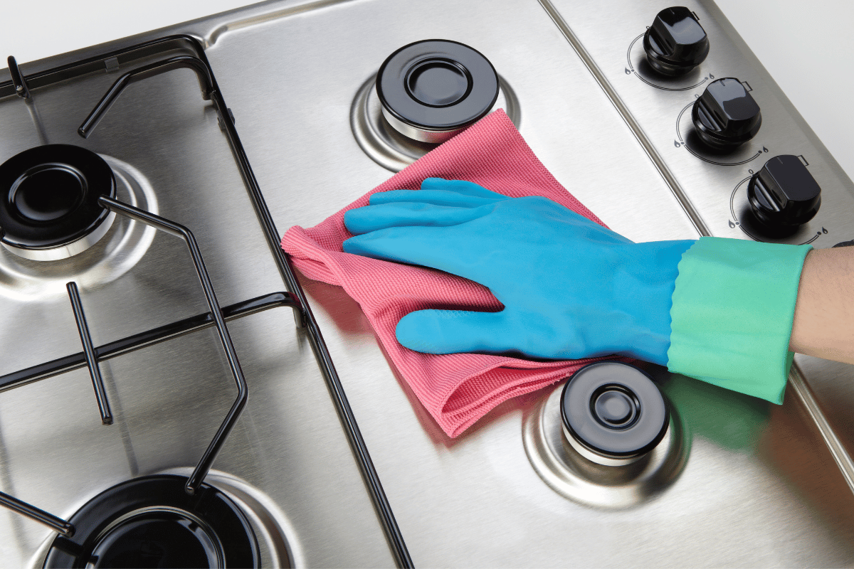 Woman cleaning set-top stove using microfiber rag and blue latex gloves.