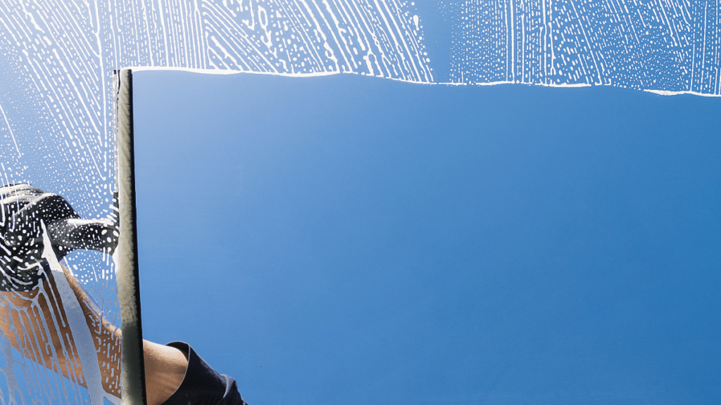 Window Cleaner Cleaning Window with Squeegee and Wiper on a Sunny day