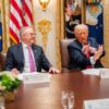 Prime Minister Anthony Albanese and President Donald J. Trump seated at a meeting table in the White House, engaged in conversation during their first official bilateral meeting, with military flags in the background.