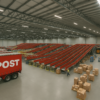 Interior of a modern Australia Post parcel-sorting facility featuring red conveyor systems, a semi-trailer truck, and neatly stacked parcels on pallets.