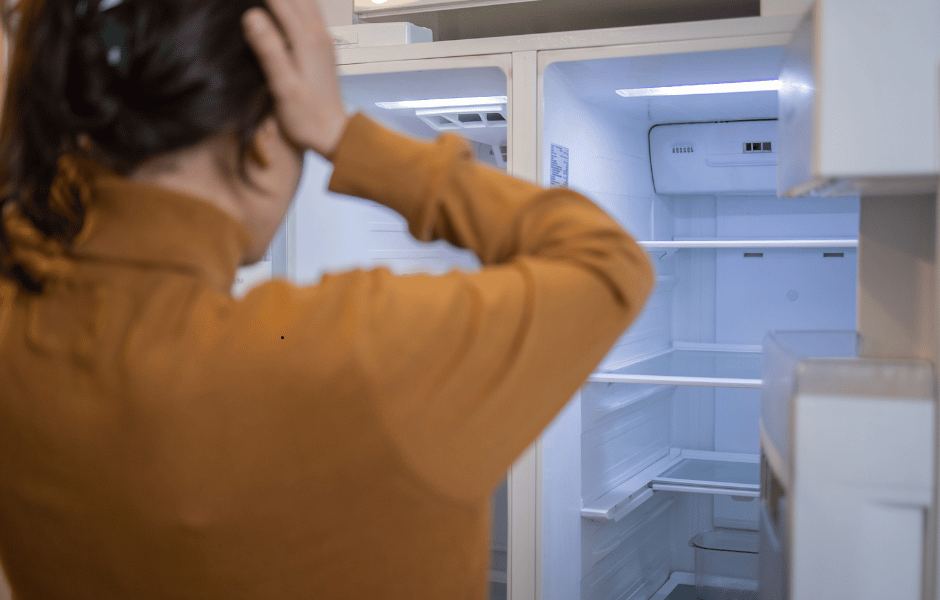 Australian woman looking into an empty fridge amid rising food costs, Foodbank Hunger Report 2025.