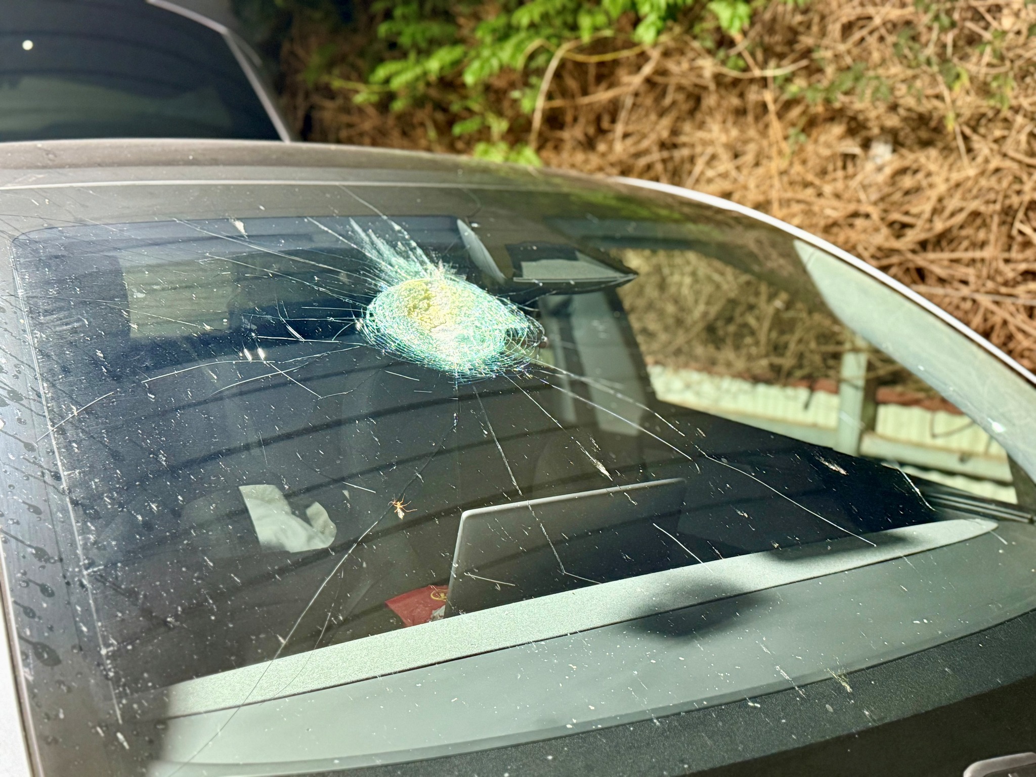 Close-up of a Tesla windshield showing a mysterious crater-like dent and melted glass, possibly caused by a meteorite impact.