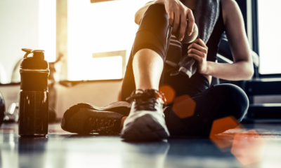 Sport woman sitting and resting after workout or exercise in fitness gym with protein shake or drinking water on floor. Relax concept. Strength training and Body build up theme. Warm and cool tone
