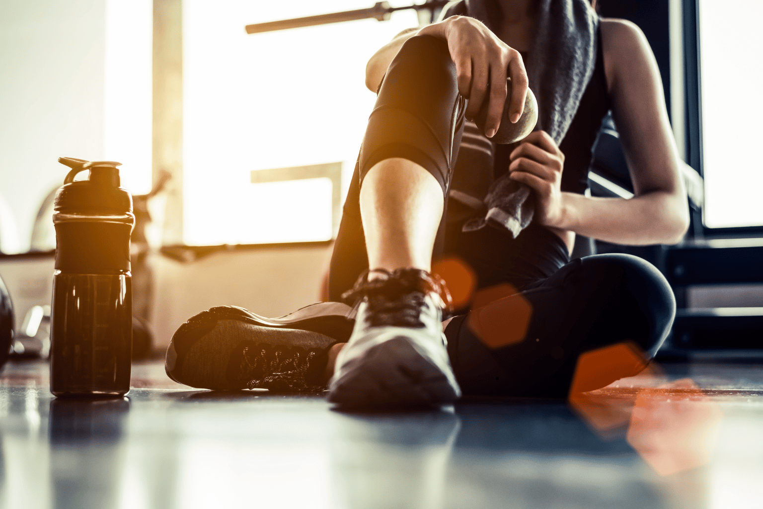 Sport woman sitting and resting after workout or exercise in fitness gym with protein shake or drinking water on floor. Relax concept. Strength training and Body build up theme. Warm and cool tone