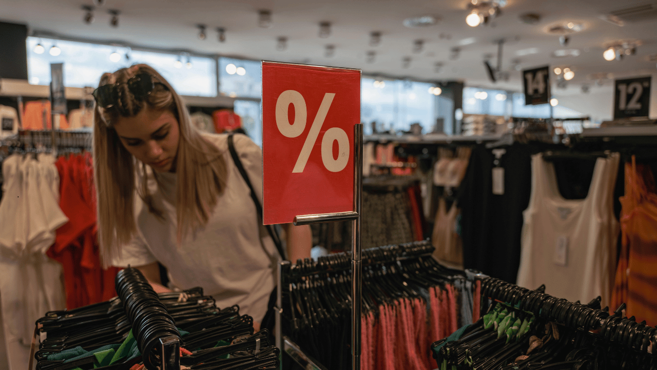 Shopper browsing discounted clothing racks, illustrating increased household spending activity.
