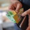 Hands holding an open wallet with Australian currency, representing household financial pressure, cost-of-living impacts, and the effects of the RBA’s interest rate decision.