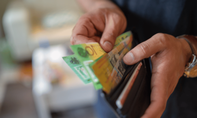Hands holding an open wallet with Australian currency, representing household financial pressure, cost-of-living impacts, and the effects of the RBA’s interest rate decision.