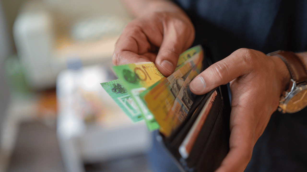 Hands holding an open wallet with Australian currency, representing household financial pressure, cost-of-living impacts, and the effects of the RBA’s interest rate decision.
