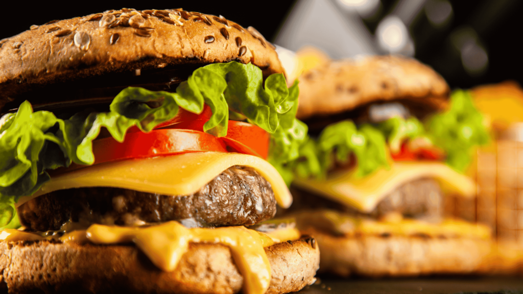 Close-up of a cheeseburger with lettuce and tomato, with another burger blurred in the background