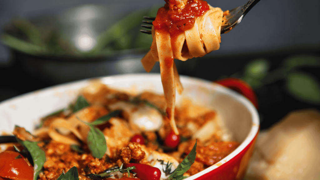 Close-up of pasta in rich tomato sauce being lifted with a fork from a bowl