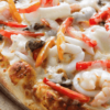 Close-up of a freshly baked seafood pizza topped with shrimp, mushrooms, cheese, and peppers.