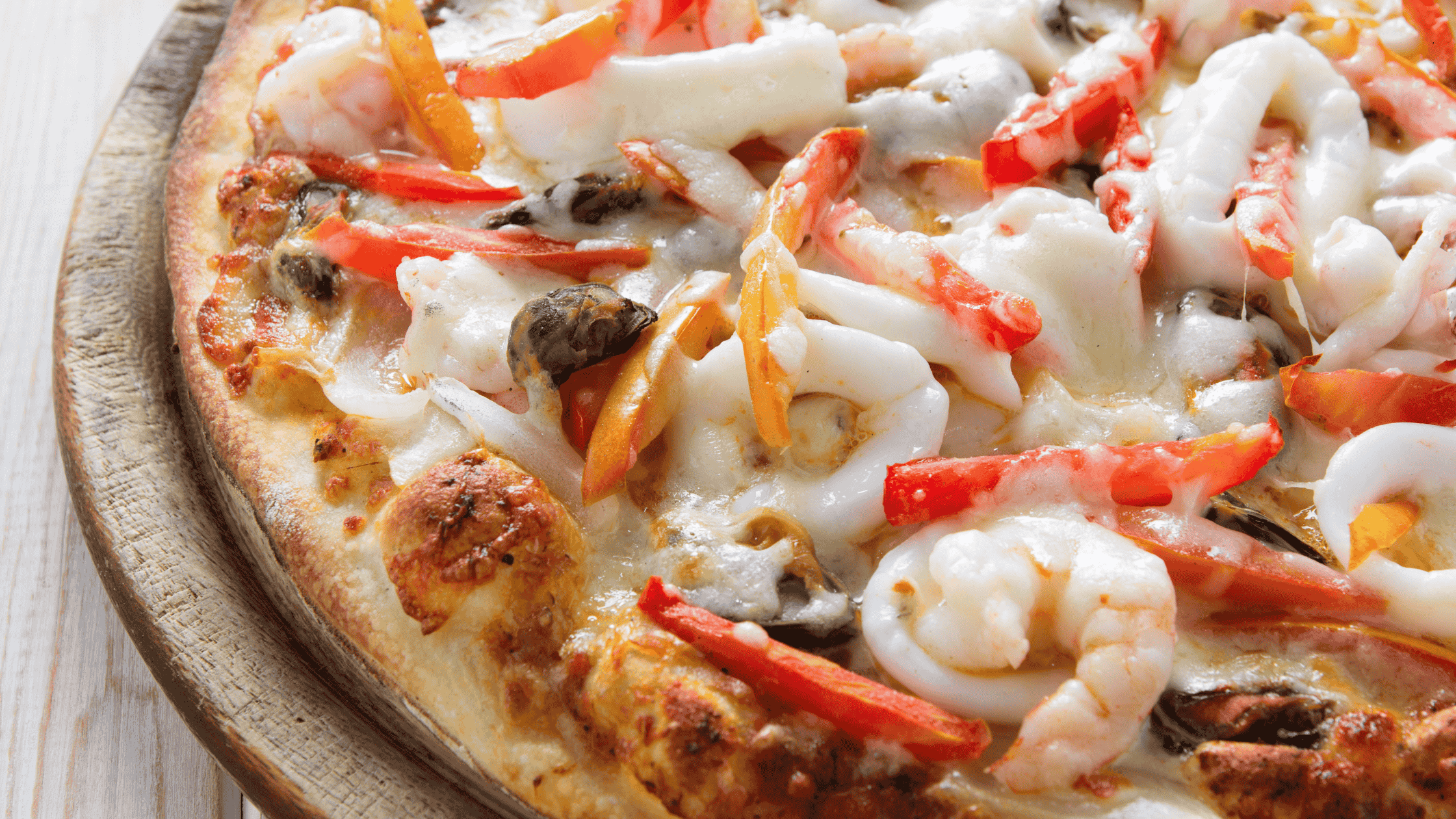 Close-up of a freshly baked seafood pizza topped with shrimp, mushrooms, cheese, and peppers.