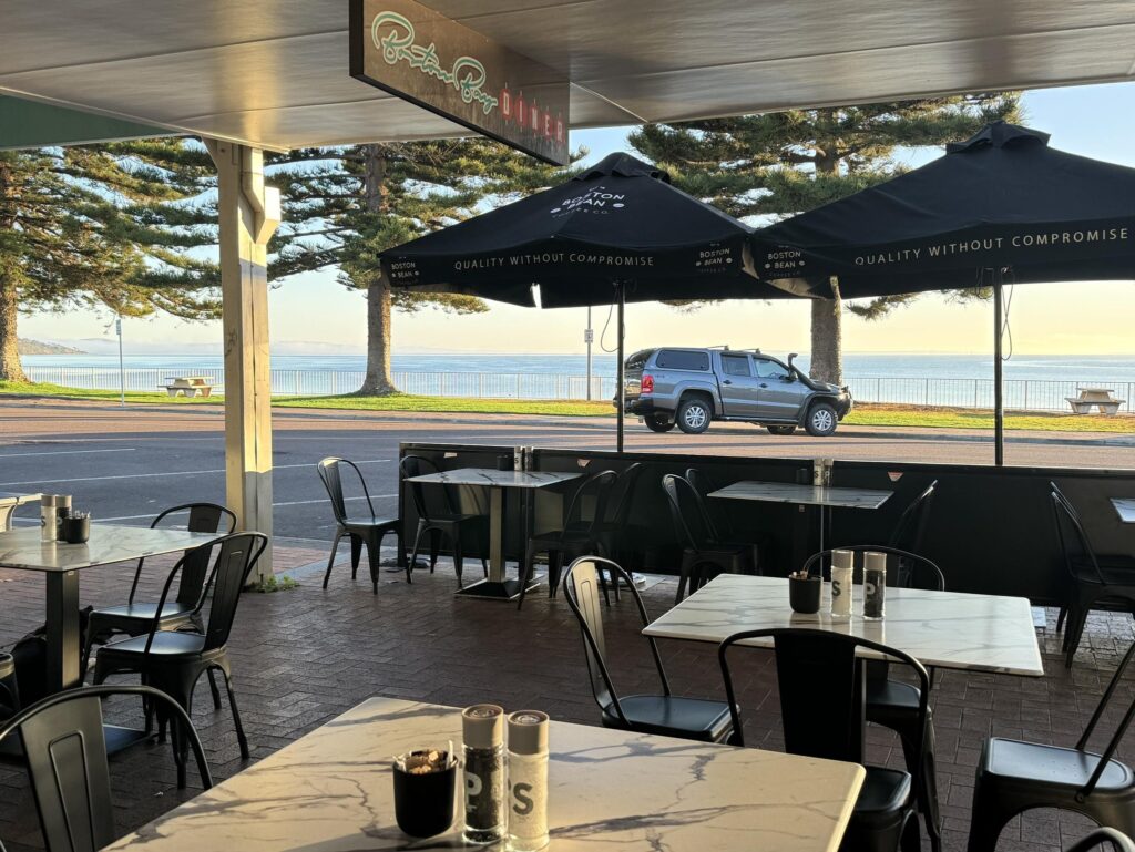 Outdoor seating area at Boston Bay Diner on the Port Lincoln foreshore, with black umbrellas, café tables, and views across the waterfront.